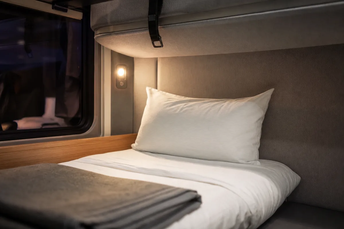 Lit superposé d&rsquo;un compartiment couchette avec drap blanc plié et petite lampe de lecture allumée
