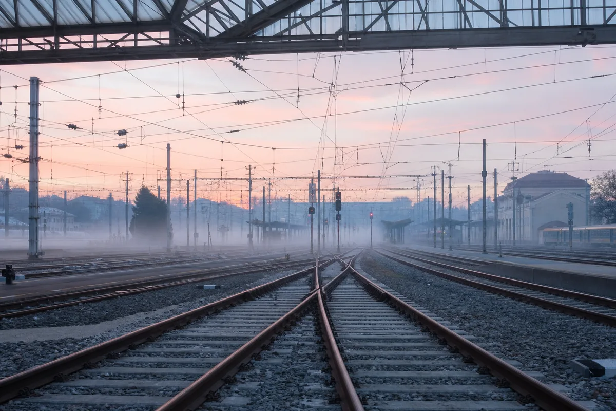 Rails et caténaires au petit matin dans une gare européenne avec brume légère